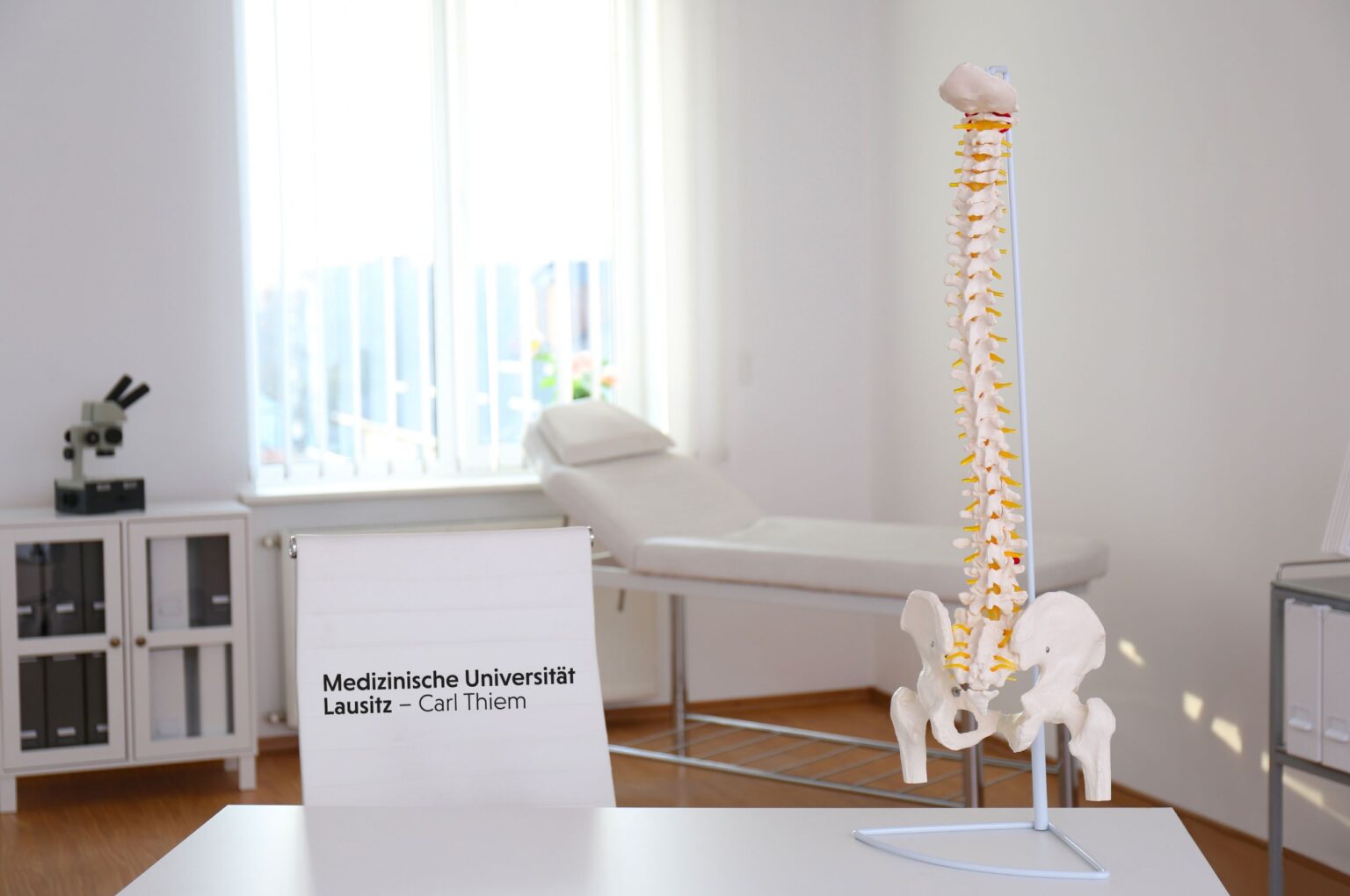 Arztzimmer mit Konochenimitat, Behandlungsliege und Block mit der Aufschrift Medizinische Universität Lausitz - Carl Thiem