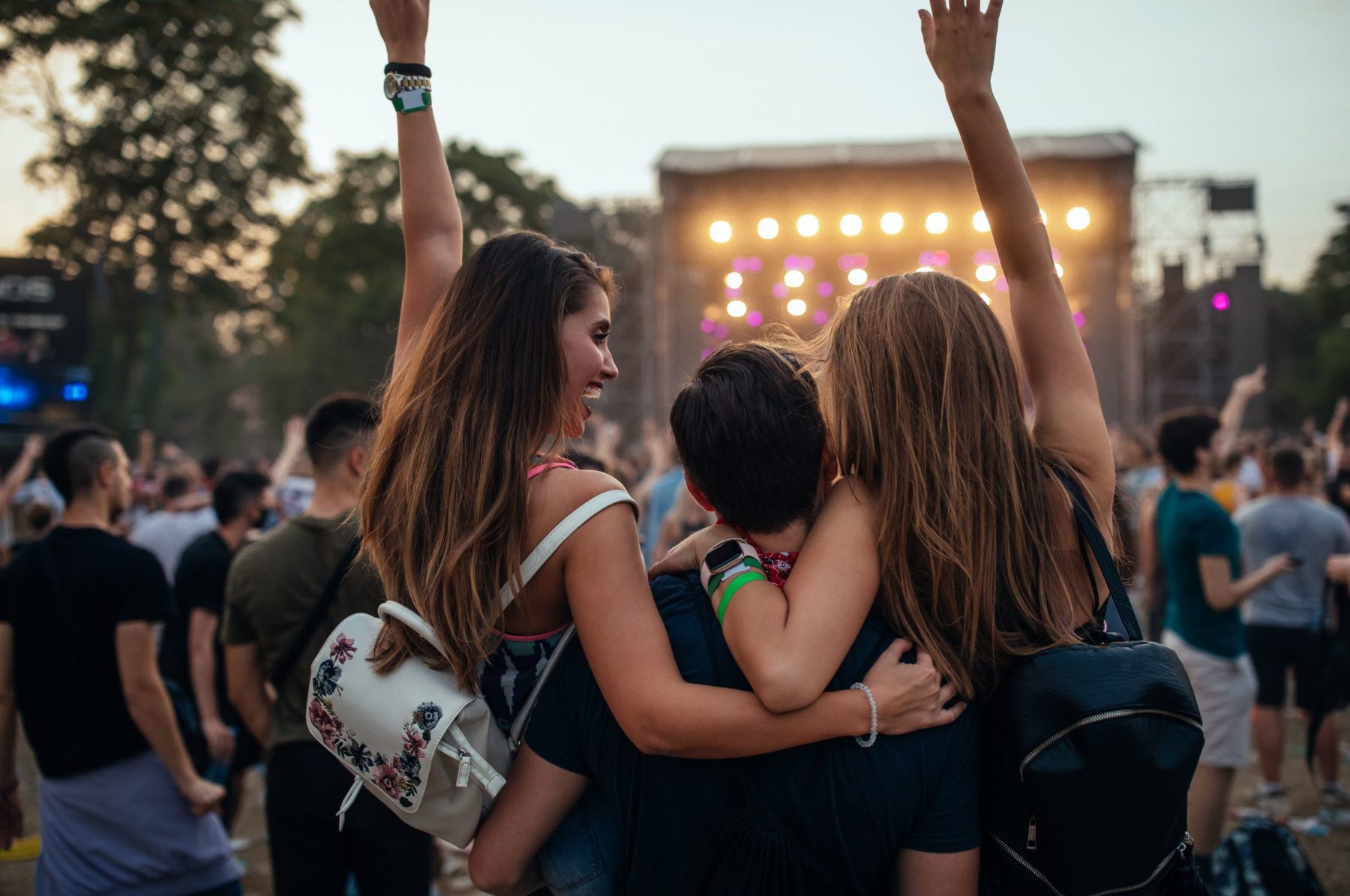Junge Menschen feiern auf einem Open-Air-Festival, umgeben von Lichtern und jubelnder Menge.