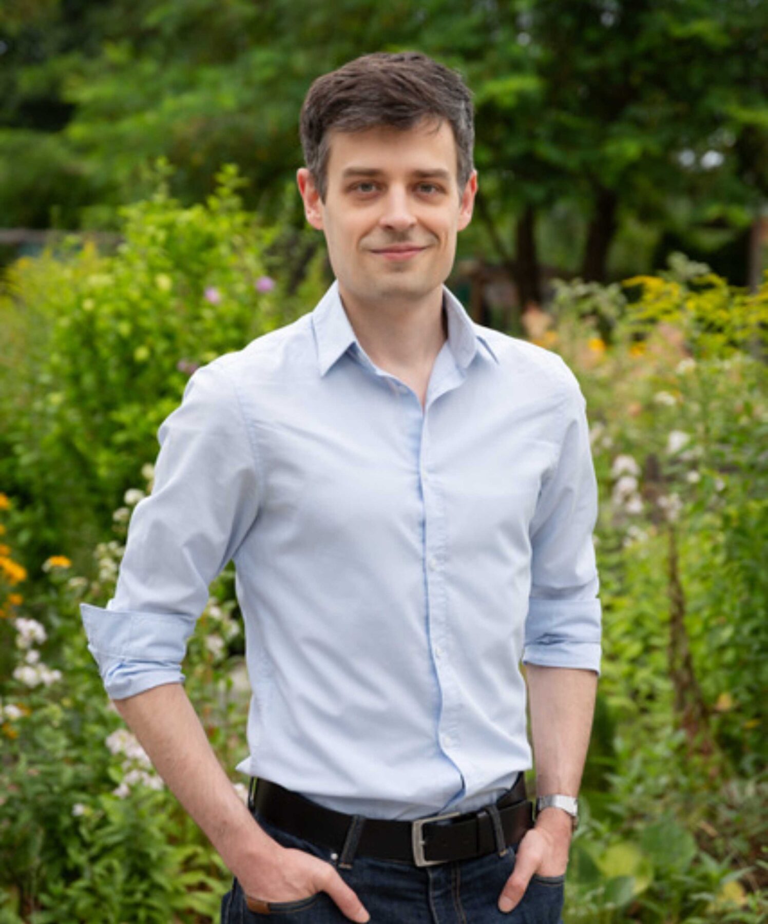 Artur, Student des Studiengangs Daten- und Informationsmanagement der Fachhochschule Potsdam im blauen Hemd steht lächelnd in einem blühenden Garten.